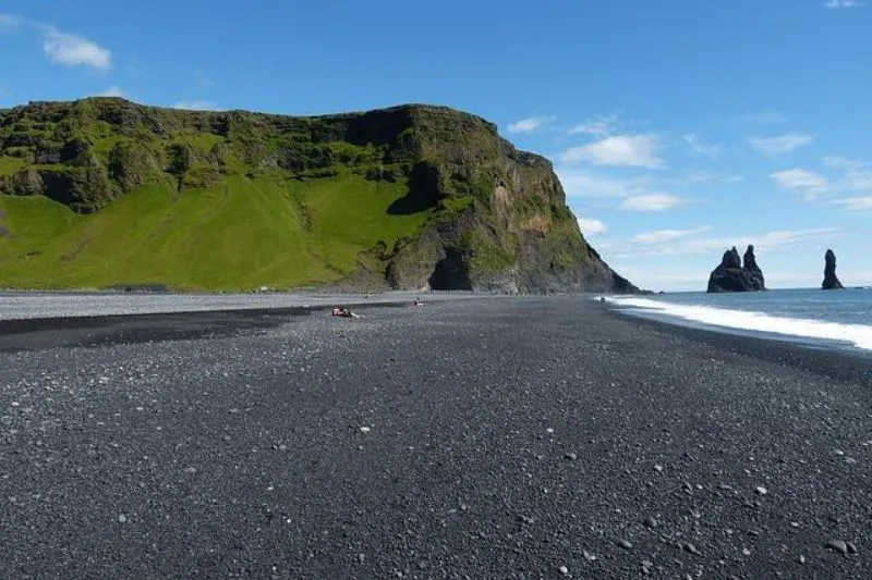 Islanda: Spiaggia di sabbia nera con scogliera verde e faraglioni sul mare