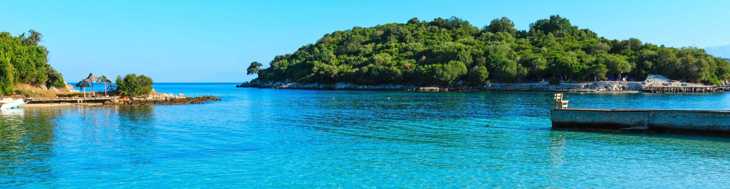 Spiaggia di Ksamil in Albania con mare cristallino, vegetazione lussureggiante e pontile in legno.
