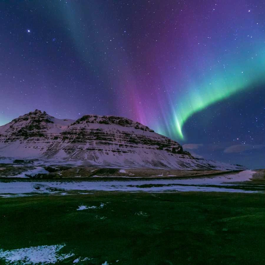 Aurora boreale sopra una montagna innevata in Islanda durante l’inverno.