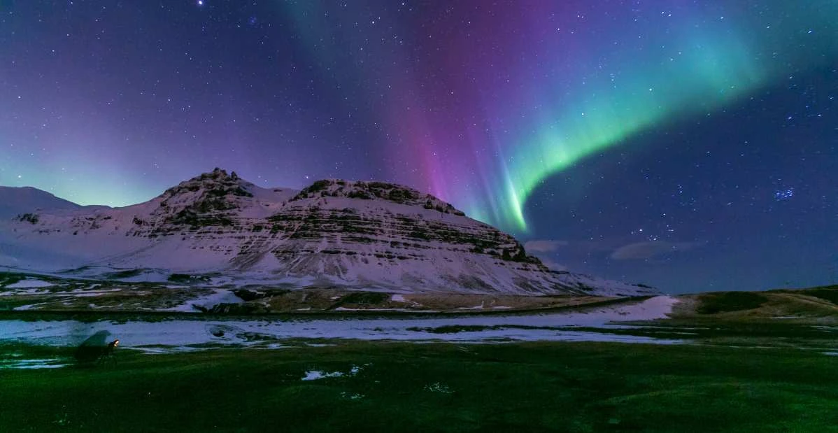 Aurora boreale sopra una montagna innevata in Islanda durante l’inverno