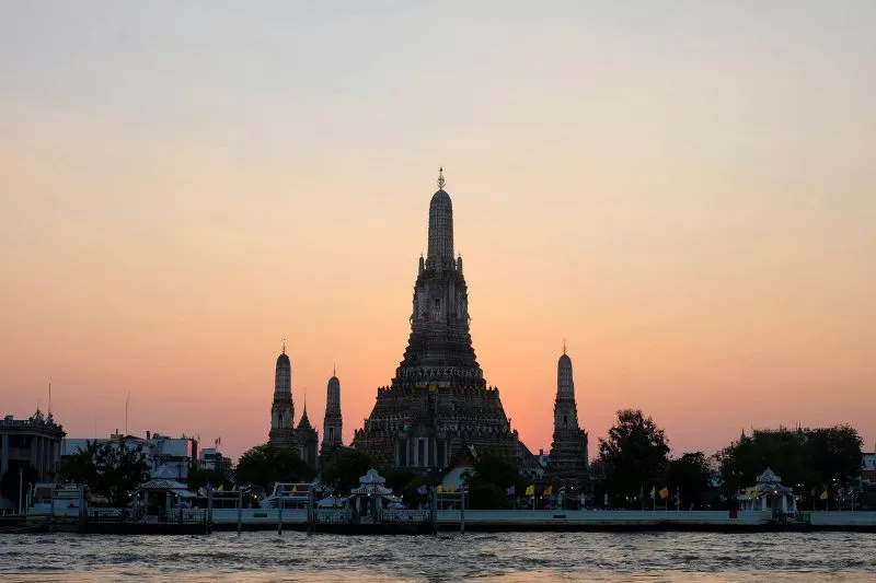 Tempio orientale illuminato dal tramonto sul fiume con cielo arancione e riflessi sull’acqua